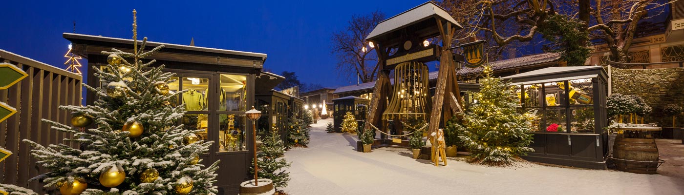 Foresta Natalizia di Lagundo: mercatino innevato con bancarelle illuminate, alberi decorati e una grande campana